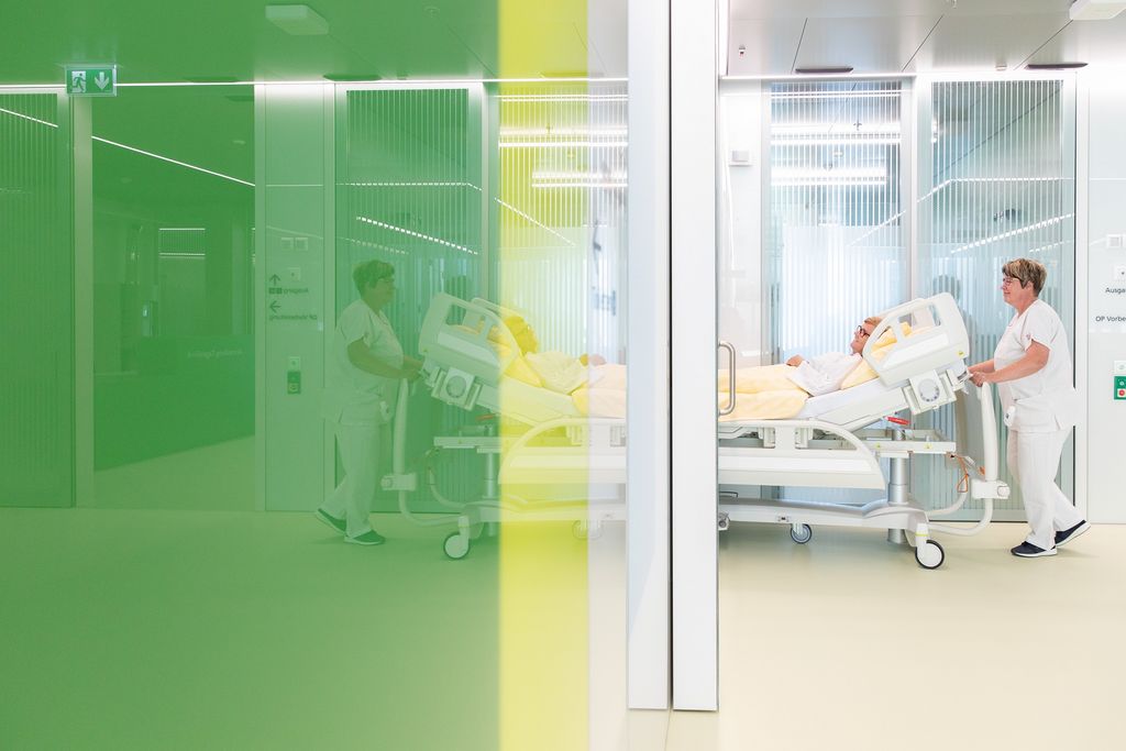 Pflegende gehen mit Patientin im Spitalbett durch den Gang 