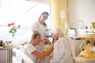 Pflege Zwei Pflegerinnen besuchen eine betagte Patientin