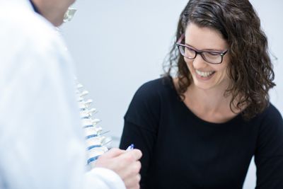 In der Wirbelsäulenchirurgie Eine Frau sieht sich lächelnd die Erklärungen des Spezialisten an.